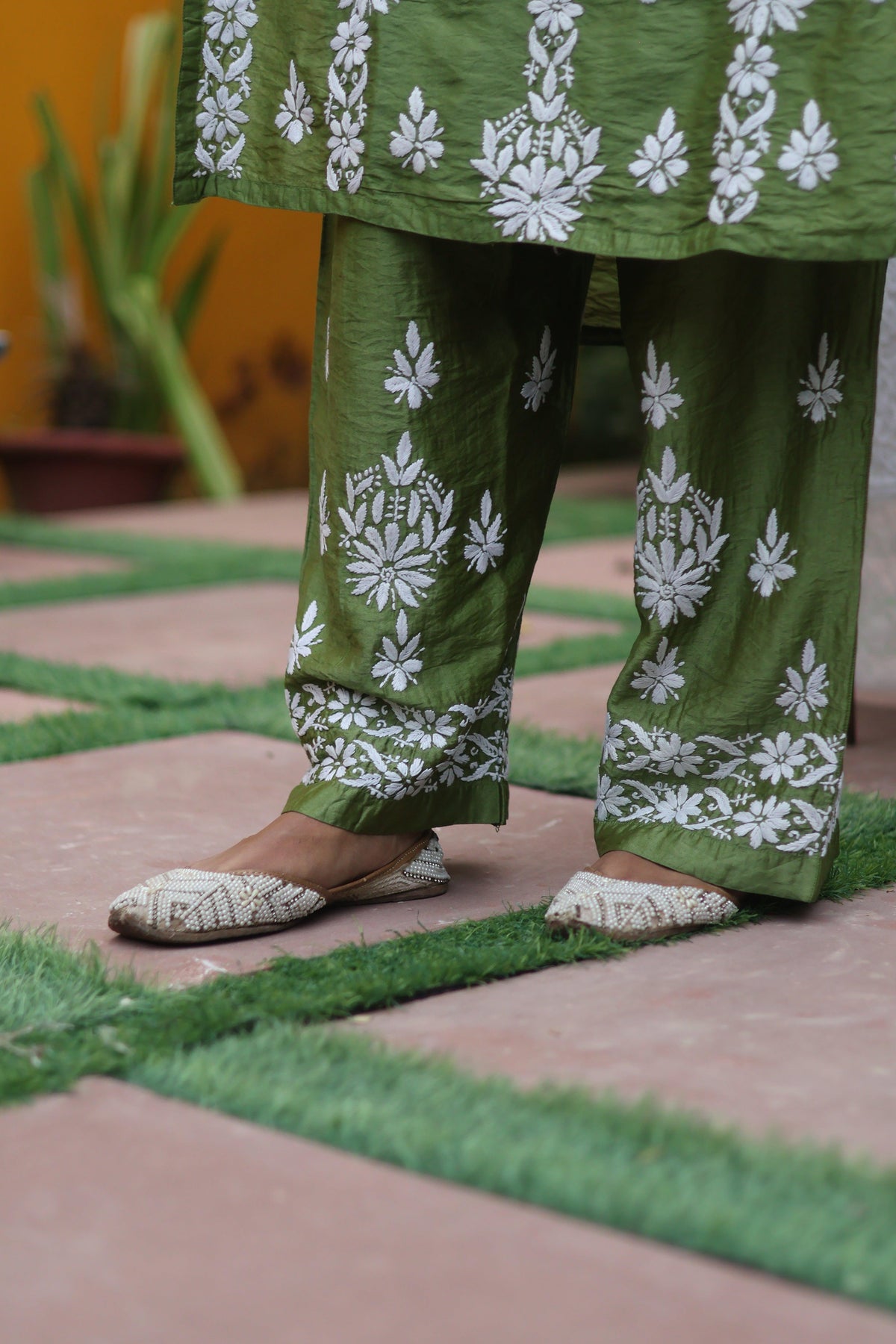 Green and white printed pants with matching flat shoes, shown on a model standing on a tiled outdoor patio.