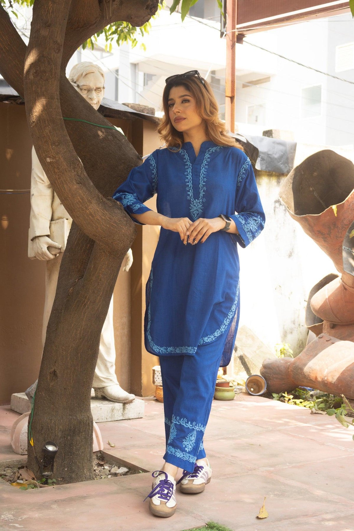 A woman modeling a royal blue two-piece kurta set with light blue embroidery, standing outdoors next to a tree. Blue Slub Cotton Chikankari Co-ord Set with White Thread Embroidery