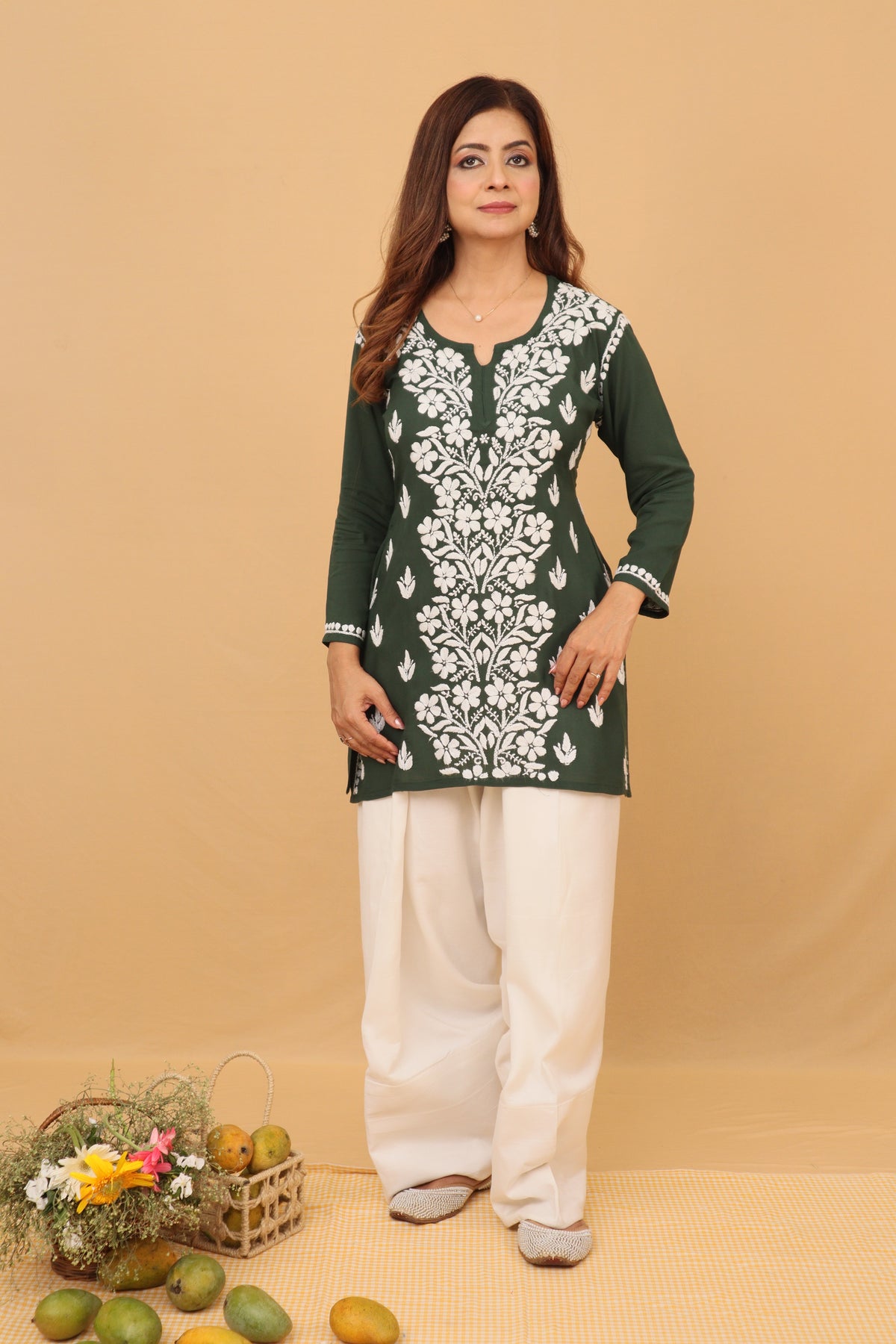 A woman modeling a dark green kurta with intricate white floral embroidery, paired with white pants, set against a solid beige backdrop.