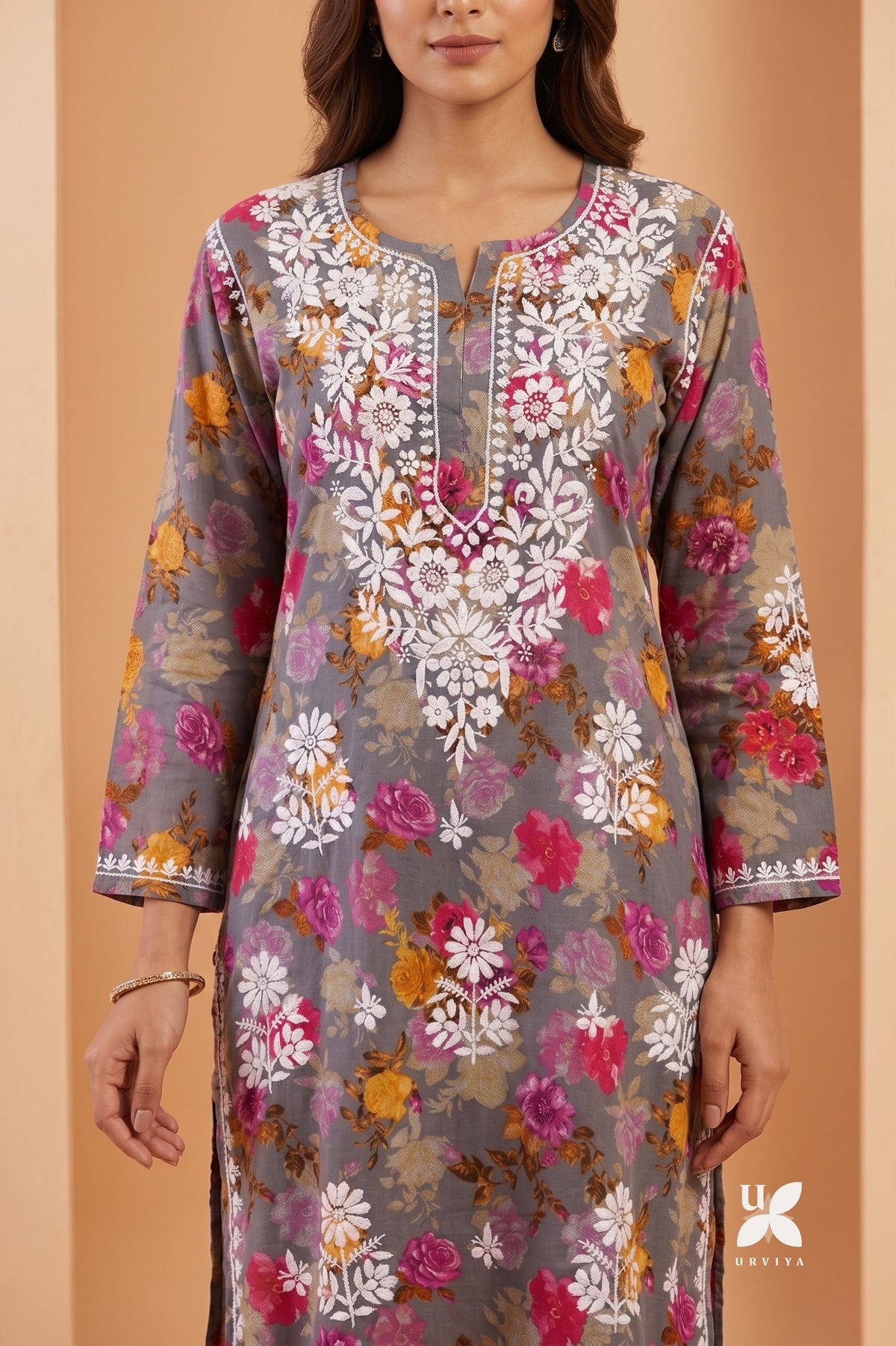 A woman wearing a gray three-quarter sleeve kurta with a vibrant multicolor floral print in pink, orange, yellow, and white, featuring white embroidered detailing around the neckline.