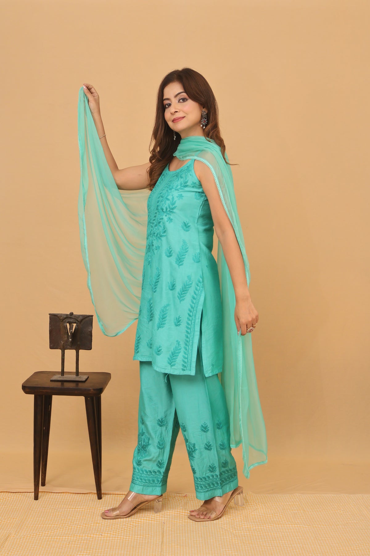 A woman models a mint green traditional Indian salwar kameez suit with matching dupatta, featuring embroidered details, standing against a solid beige backdrop.
