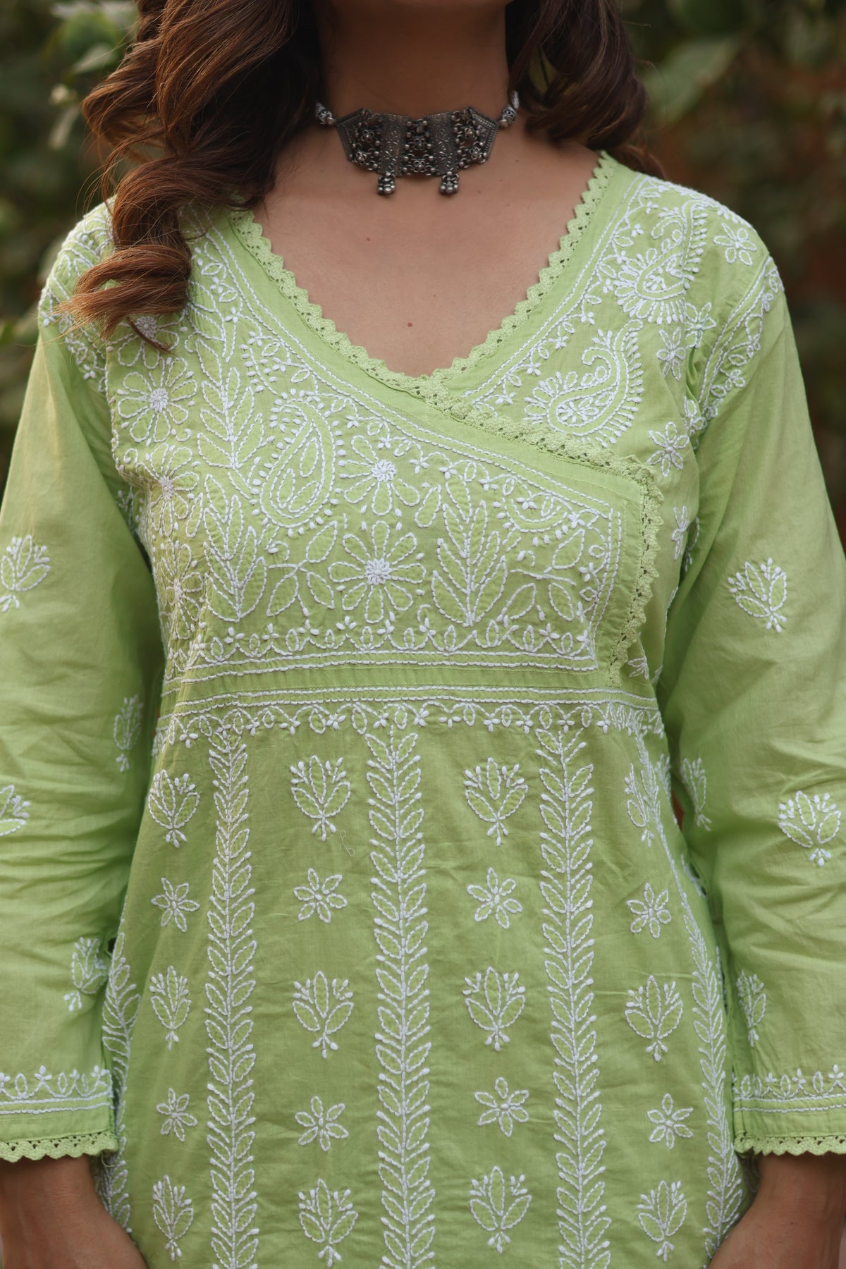 A close-up of a woman wearing a light green cotton kurta with intricate white floral and paisley embroidery, featuring a V-neckline and 3/4 sleeves.