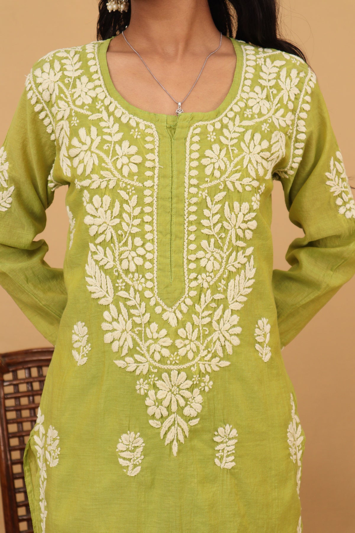 A lime green cotton kurta with intricate off-white floral embroidery on the front, shown on a model against a warm beige background.