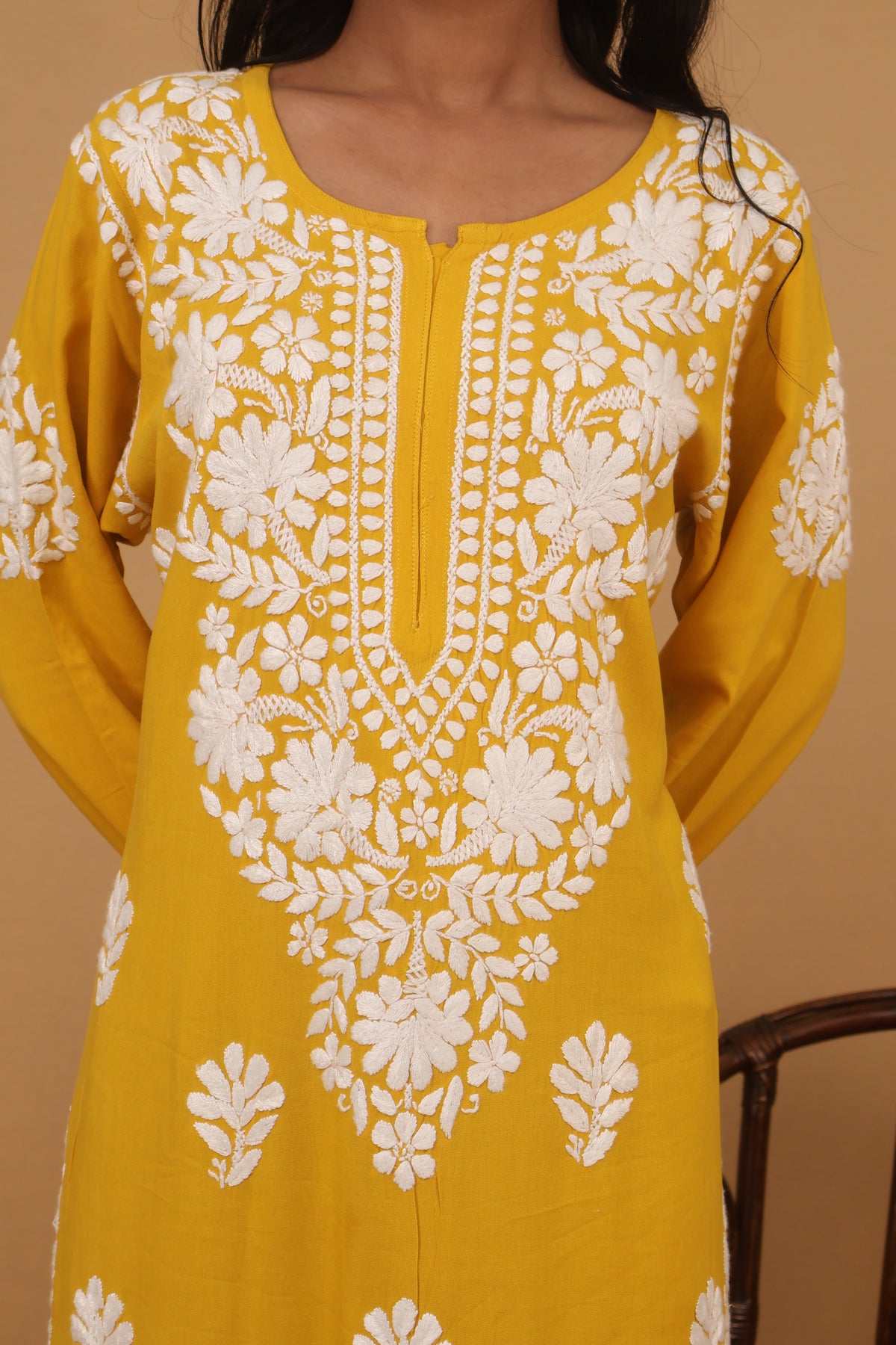 A close-up of a mustard yellow kurta with intricate white floral embroidery and border detailing, shown on a model.