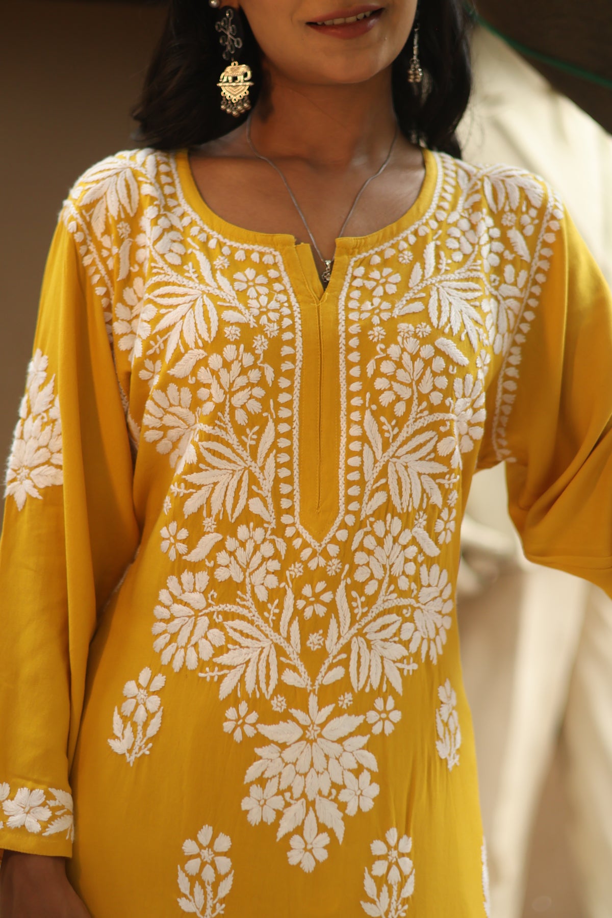 A close-up of a woman wearing a yellow kurta with intricate white floral embroidery and a split neckline.