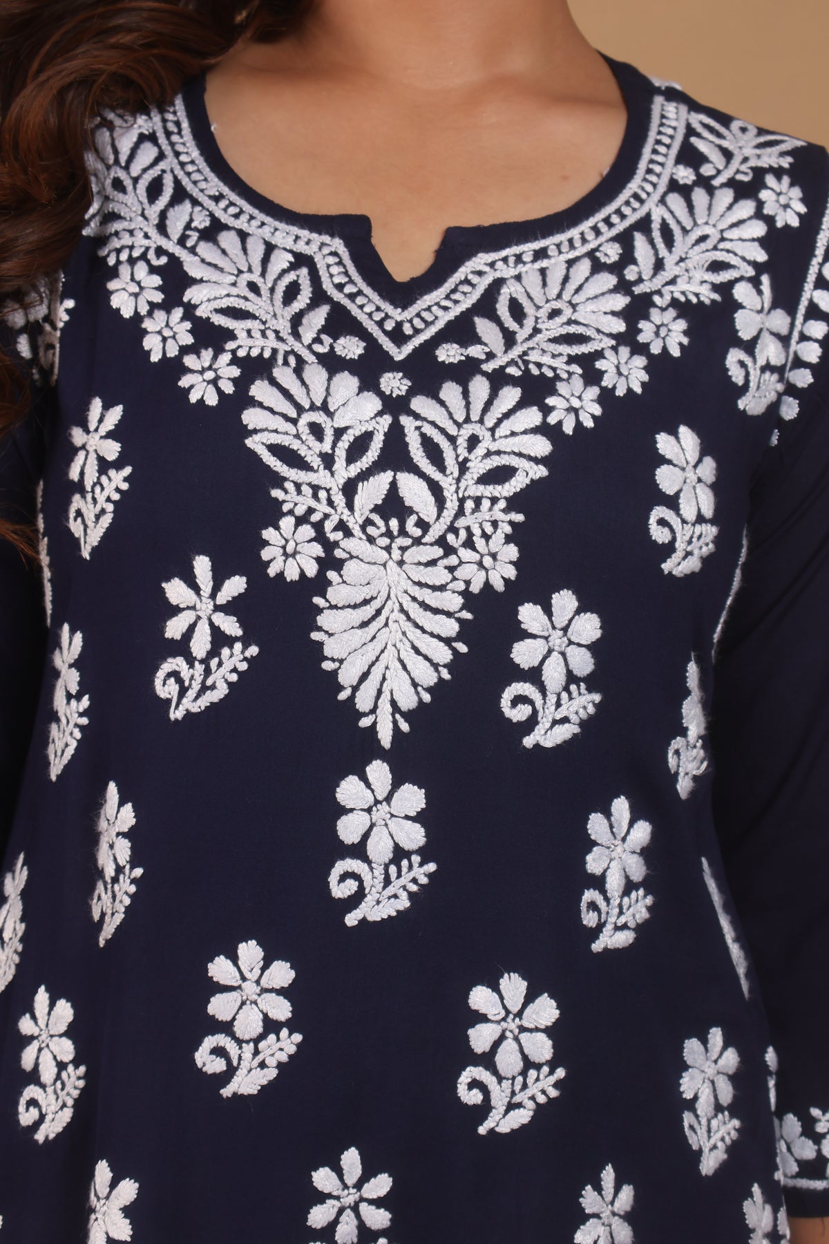A close-up of a navy blue tunic top with intricate white floral embroidery and a split neckline, worn by a model.