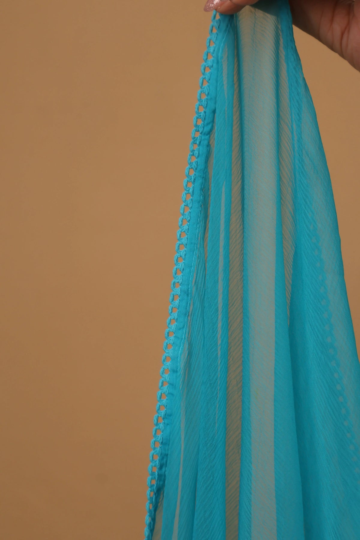 A close-up of a sheer turquoise blue fabric, likely a dupatta or scarf, held by a hand against a solid tan background.