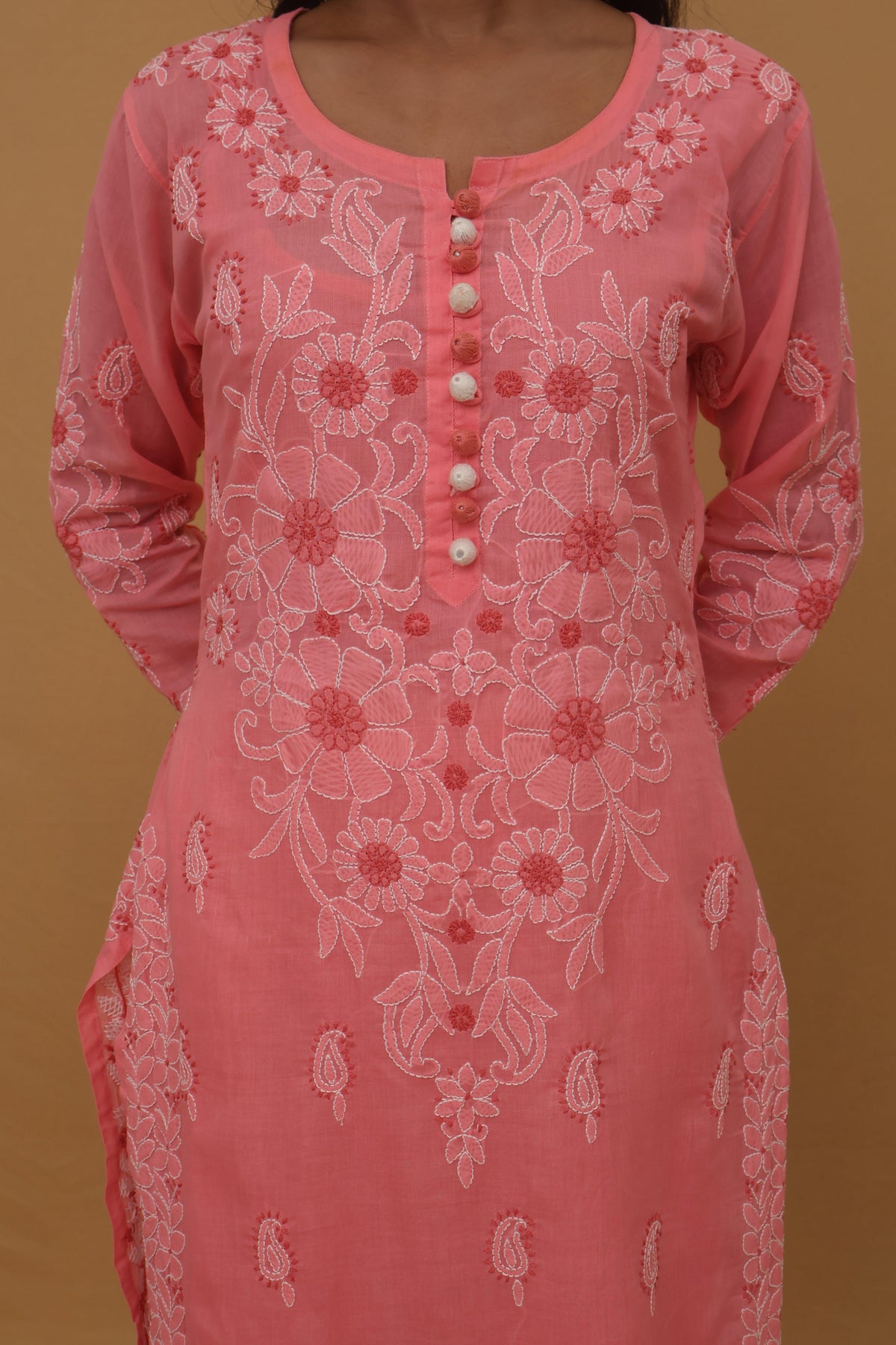 A pink long-sleeve kurta with white floral embroidery and a buttoned neckline, shown on a model against a solid tan background.