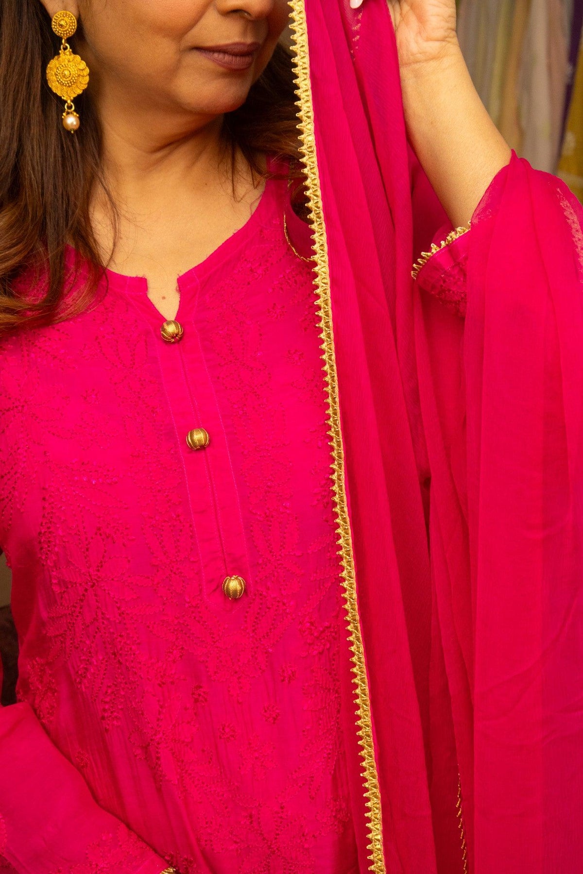 A close-up of a woman wearing a bright pink embroidered kurta with gold buttons and a matching sheer pink dupatta with a gold embroidered border. Pink Muslin Chikankari Bakhiya 2 Piece Set with Golden Gotta Lace