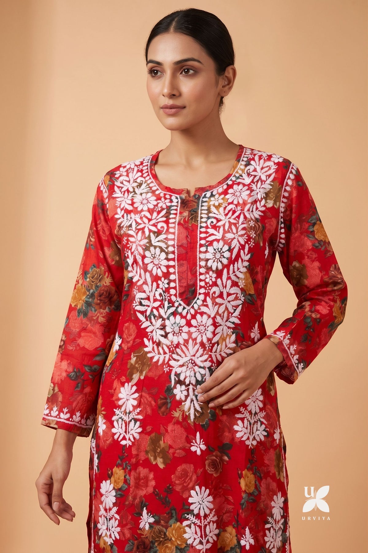A woman modeling a red long-sleeve kurta with white floral embroidery and a multicolor floral print, set against a solid beige background.