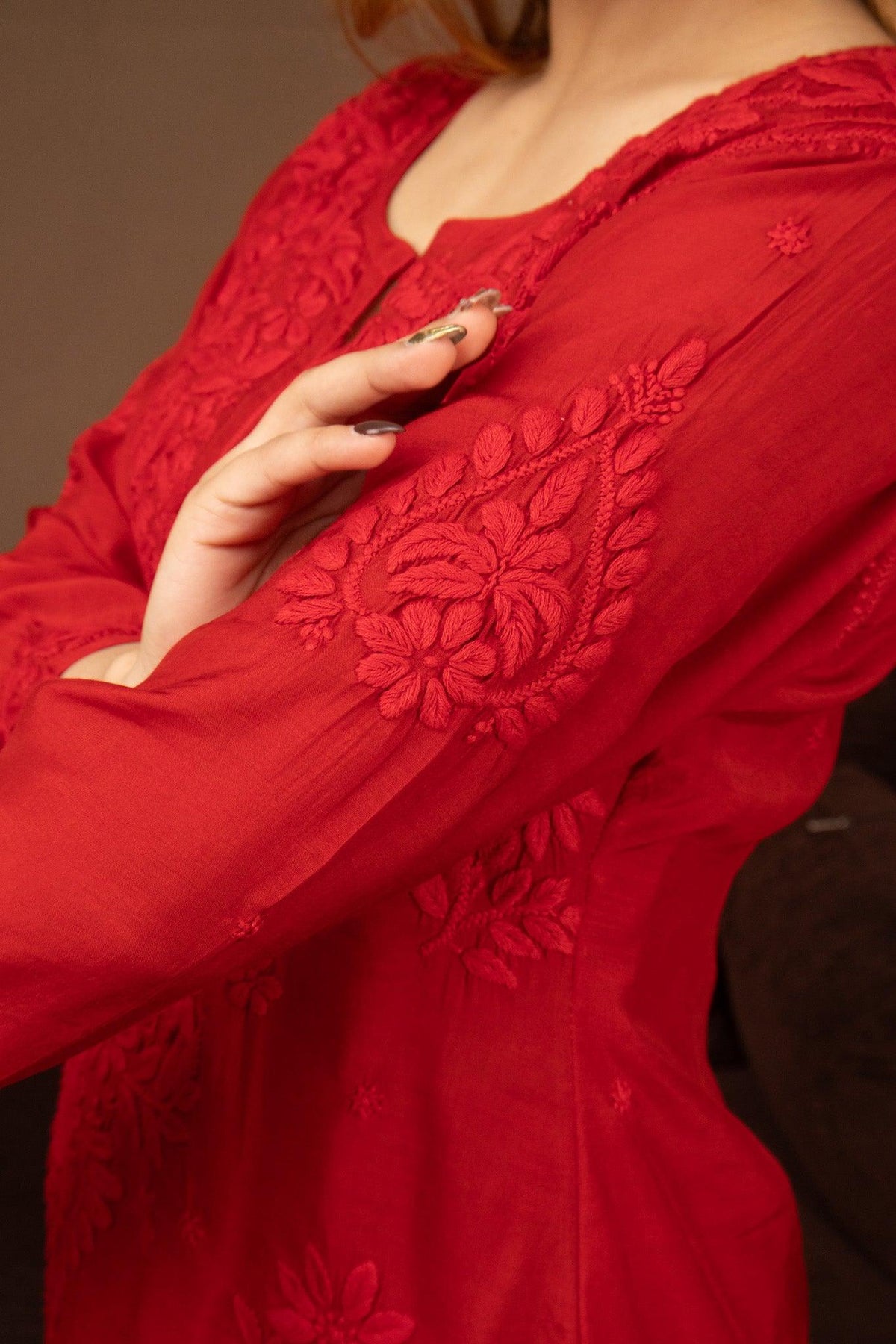 A close-up of a person wearing a vibrant red long-sleeve kurta with intricate floral embroidery and lace detailing on the chest and sleeves. Red Muslin Chikankari Ghaaspatti Long Kurti with Tone-on-Tone Embroidery