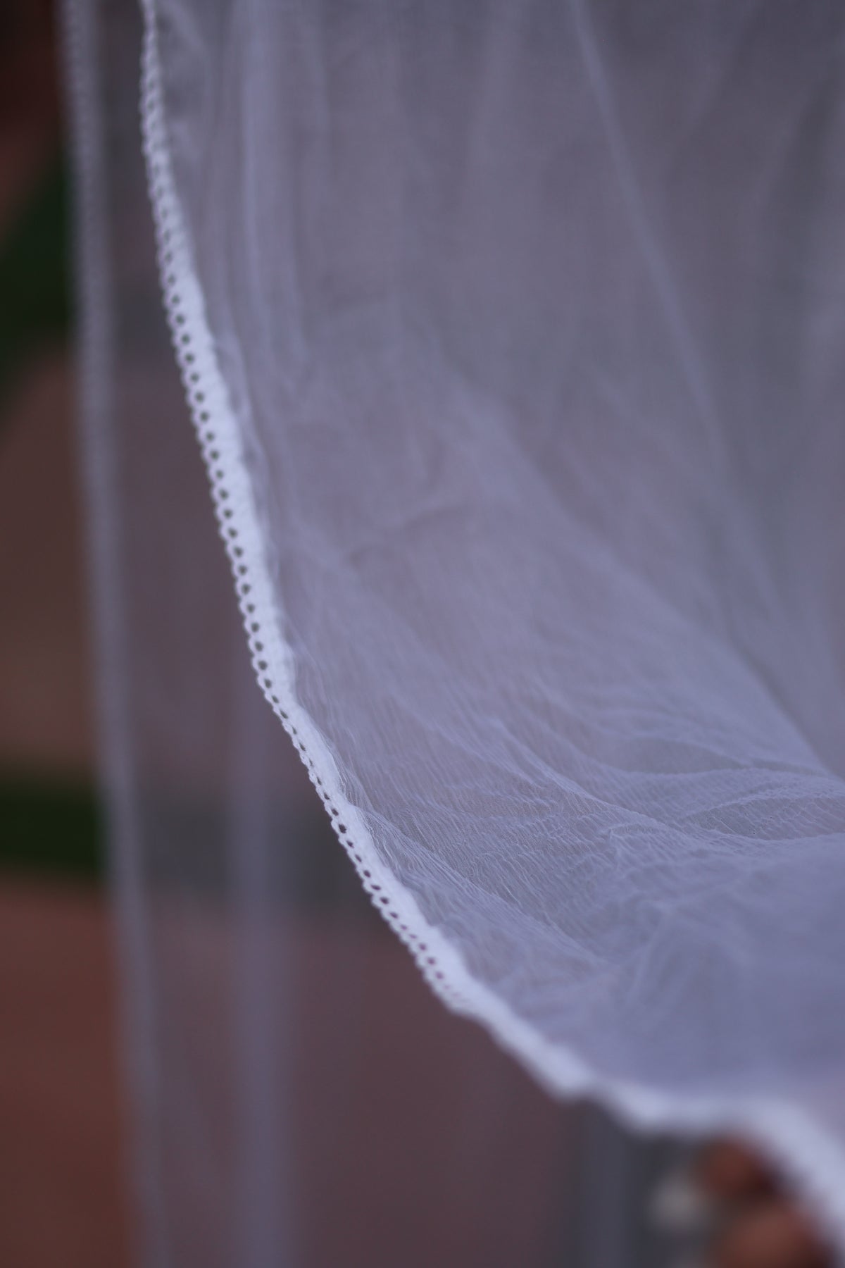 A close-up of a white tulle bridal veil with a delicate lace trim, draped against a softly blurred background.