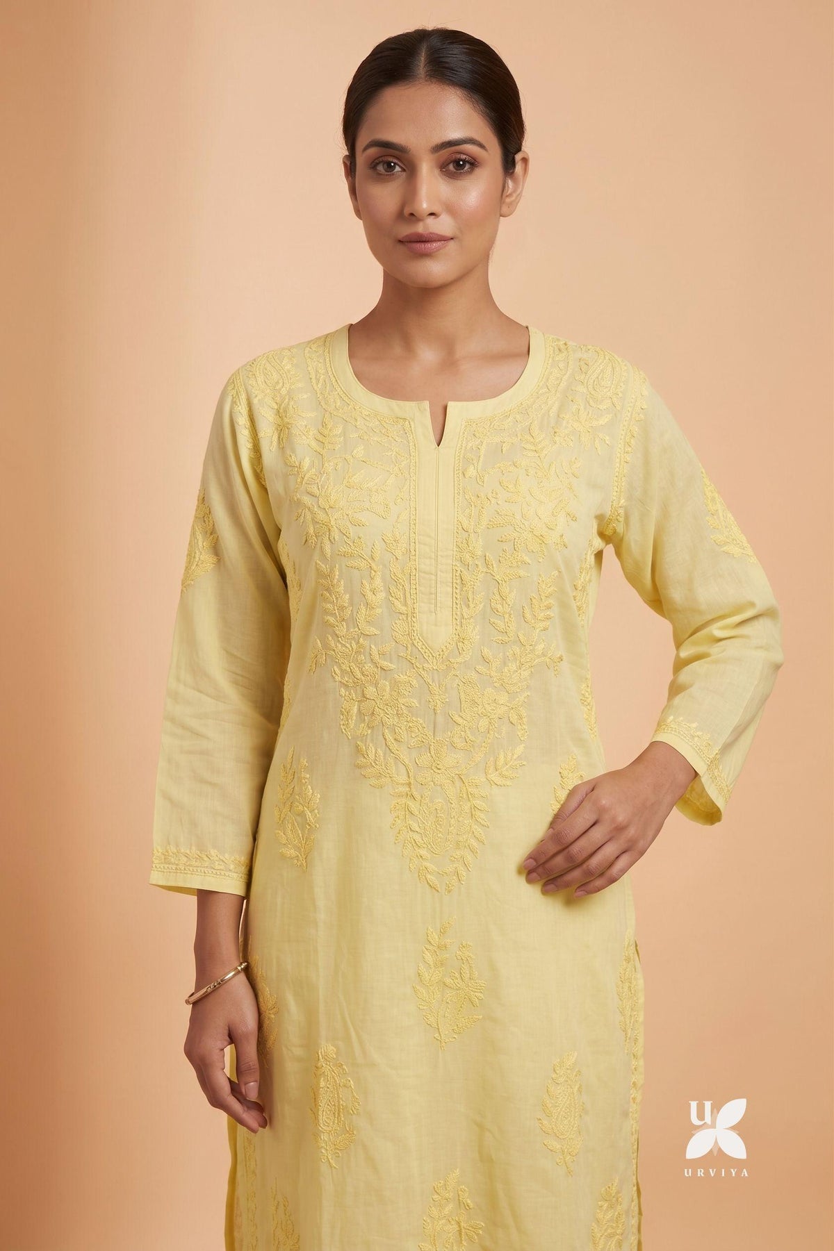 A woman modeling a light yellow embroidered kurta with three-quarter sleeves and a split neckline, set against a solid peach background. A small 'ULTRA' brand logo is visible in the bottom right corner.
