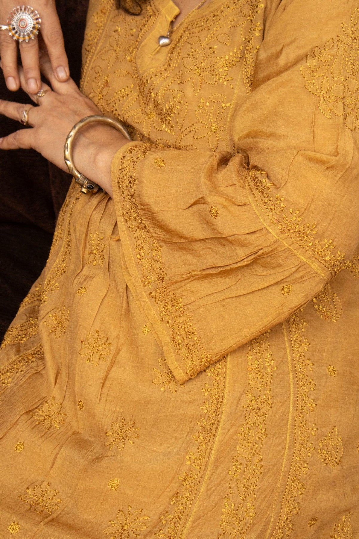 A close-up of a mustard yellow embroidered traditional outfit with long sleeves, featuring intricate floral embroidery and lace detailing on the fabric and cuffs. Yellow Muslin Nyra Cut Chikankari Kurti with Bakhiya Embroidery